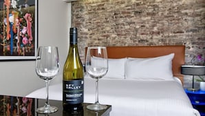 A hotel room with a bed, a brick wall, and a painting. There is a bottle of wine and two glasses on a table. - Boutique Unit Near Ferry Building, Powell BART & SFMOMA (San Francisco)