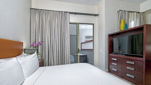 Ein Hotelzimmer mit einem großen Bett, einer Holzkommode mit Schubladen, einem Fernseher und einem Fenster mit Vorhängen.