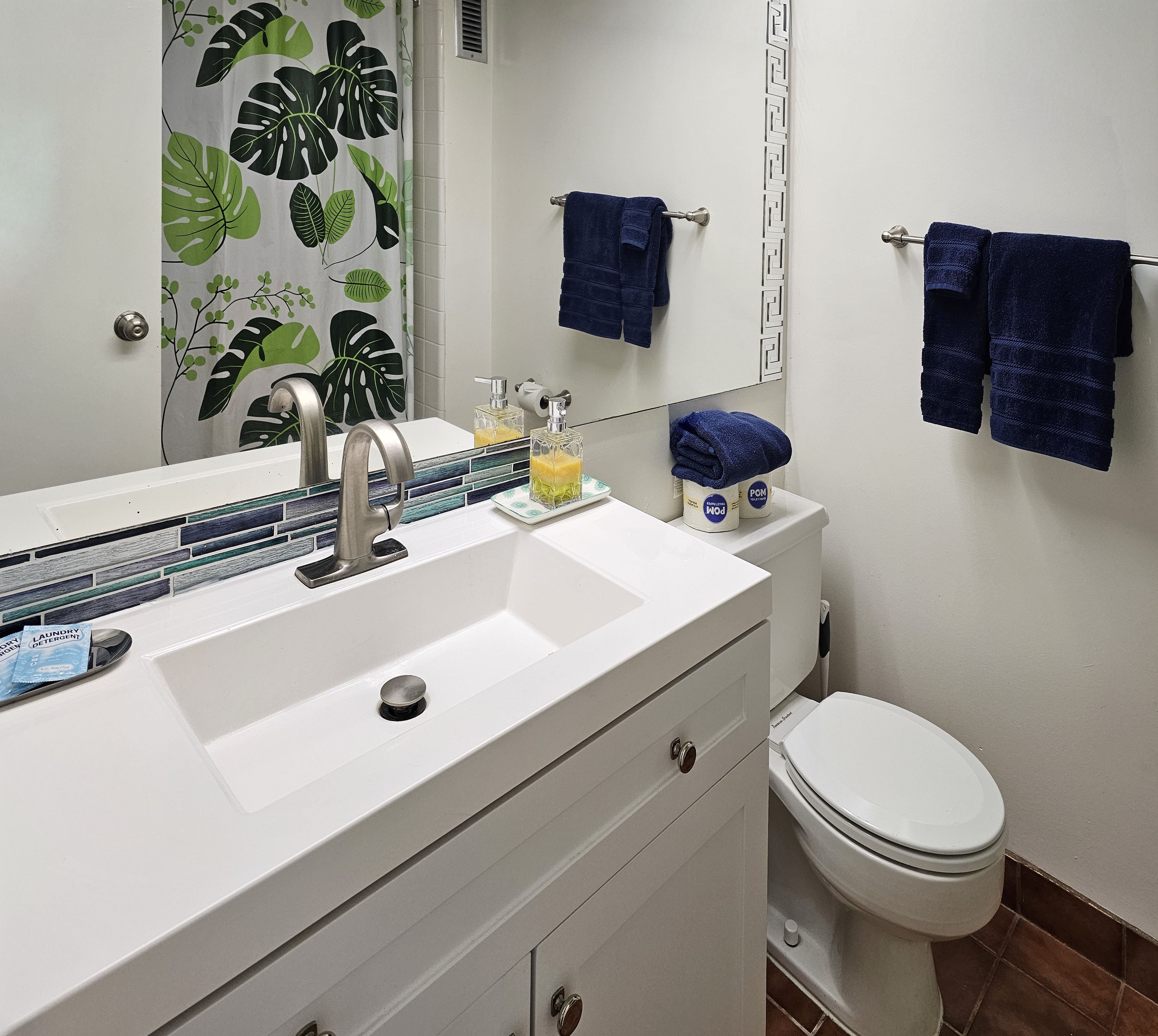 A bathroom with a white sink, a mirror, a toilet, and blue towels hanging on the wall.