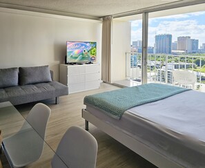 A modern hotel room with a bed, sofa, TV, and a balcony with a city view. - Free parking, Partial ocean view, 18th FL, Renovated (Honolulu)