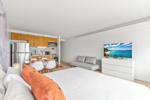 A modern hotel room with a large bed, a grey sofa, a dining area with a kitchen, and a TV on the wall. - Free parking, Partial ocean view, 18th FL, Renovated (Honolulu)