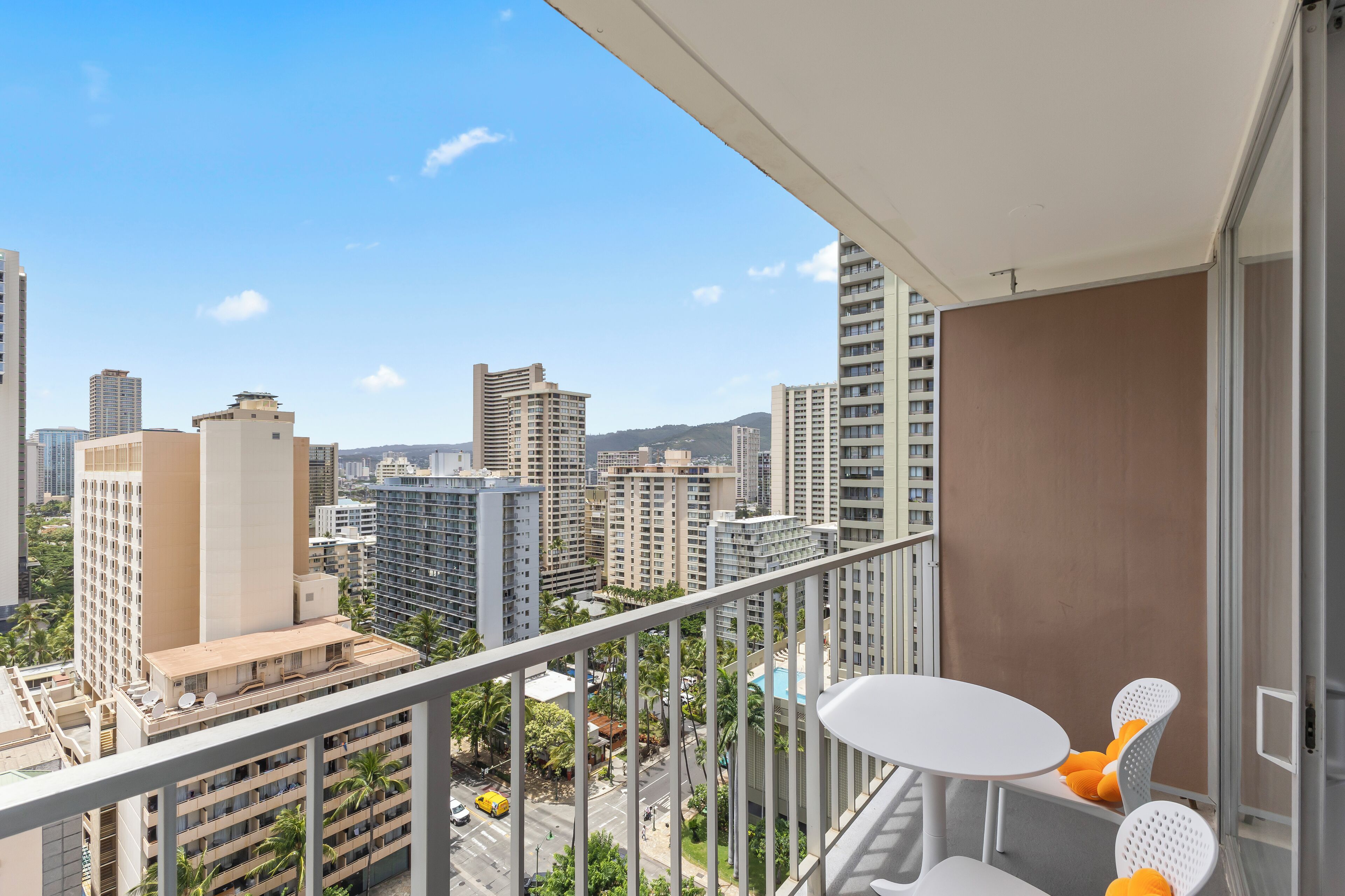A balcony with a white table and chairs, overlooking a cityscape with high-rise buildings and palm trees.