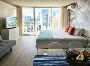 Ein Hotelzimmer mit Bett, Fernseher, Sitzgelegenheit und Blick auf die Stadtlandschaft.