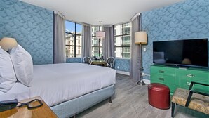 A hotel room with a large bed, a TV, a desk with two chairs, and a green dresser. - Elegant Unit with Rooftop Pool at SoMa House, Walk to Civic Center (San Francisco)