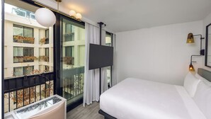 A hotel room with a large bed, a TV, a balcony with a view of other buildings, and a modern light fixture. - Poolside Relaxation in Hollywood with Rooftop & Pet-Friendly (Los Angeles)