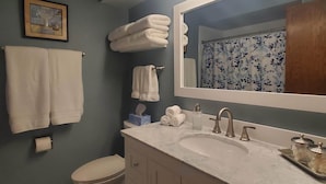 Een badkamer met een witte wastafel, een spiegel en een toilet. Handdoeken hangen aan de muur en er staat een fotolijst.