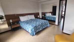 Une chambre d’hôtel avec un lit double, une table de chevet avec une lampe, une chaise et un grand miroir.