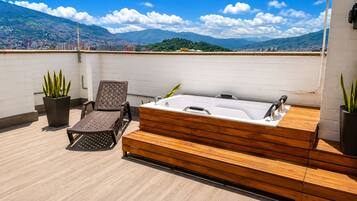 Una terraza en la azotea con cubierta de madera, un jacuzzi y dos sillones de descanso.