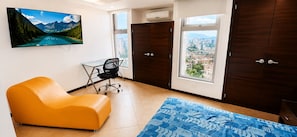A room with a large window, a desk, an orange chair, and a bed with a blue patterned bedspread. - Penthouse Rooftop  Gem in the Laureles (Medellín)