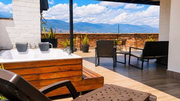 A rooftop terrace with a wooden bench, a hot tub, and a table with chairs.