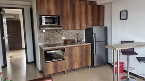 Une cuisine compacte avec des meubles en bois, un four à micro-ondes encastré, un réfrigérateur en acier inoxydable, un petit four et un tabouret de bar.
