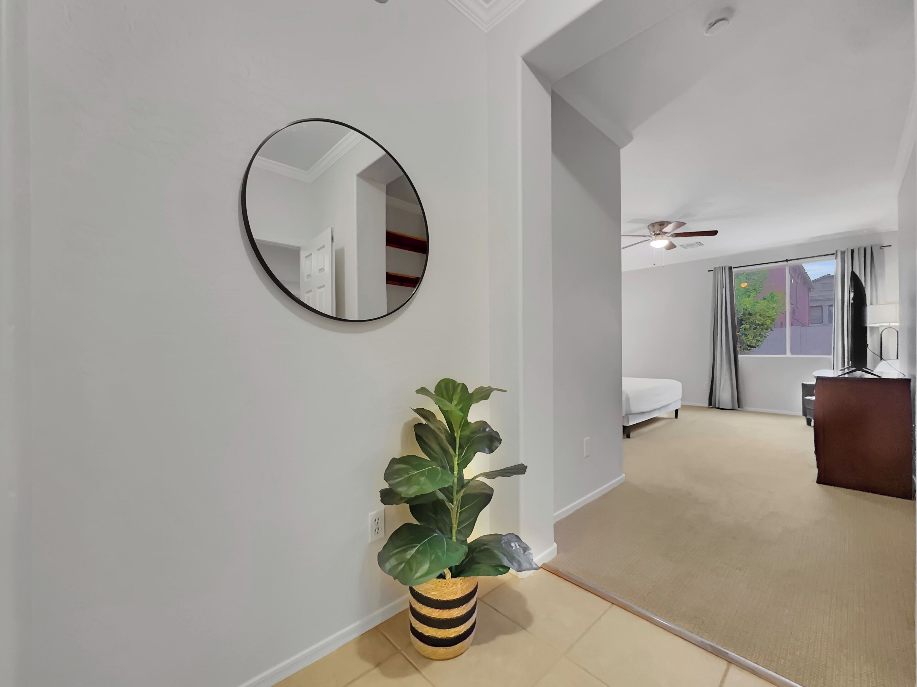 A hotel room with a large mirror, a potted plant, a bed, a desk, and a ceiling fan.