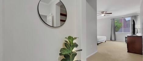 A hotel room with a large mirror, a potted plant, a bed, a desk, and a ceiling fan.