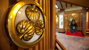 A traditional Japanese interior with a decorative golden emblem, wooden paneling, and a patterned floor. - Hitomarukadan (Akashi)