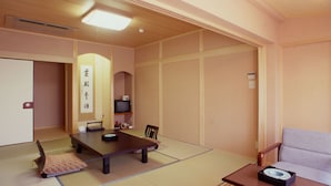 A traditional Japanese room with tatami flooring, a low table, a sofa, and a television. - Hitomarukadan (Akashi)
