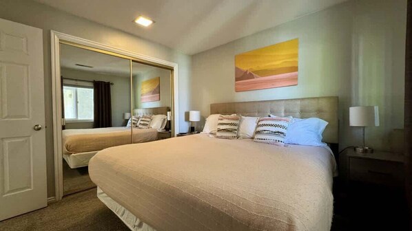 A hotel room with a large bed, a mirror, a painting on the wall, and a nightstand with a lamp.