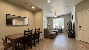 A spacious living area with a dining table, chairs, a sofa, and a ceiling fan.