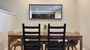 A dining area with a rectangular table, two chairs, a small potted plant, and a mirror on the wall.