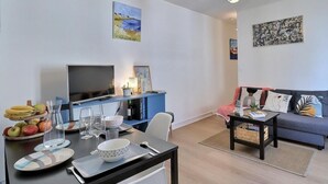 A modern living room with a dining area, a sofa, and a TV. There are fruits on the table, a bookshelf, and artwork on the walls. - Herman's stopover - SAINT MALO (SAINT MALO)