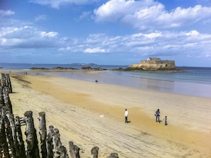 Ein sandiger Strand mit einem historischen Steinhaus im Hintergrund.
