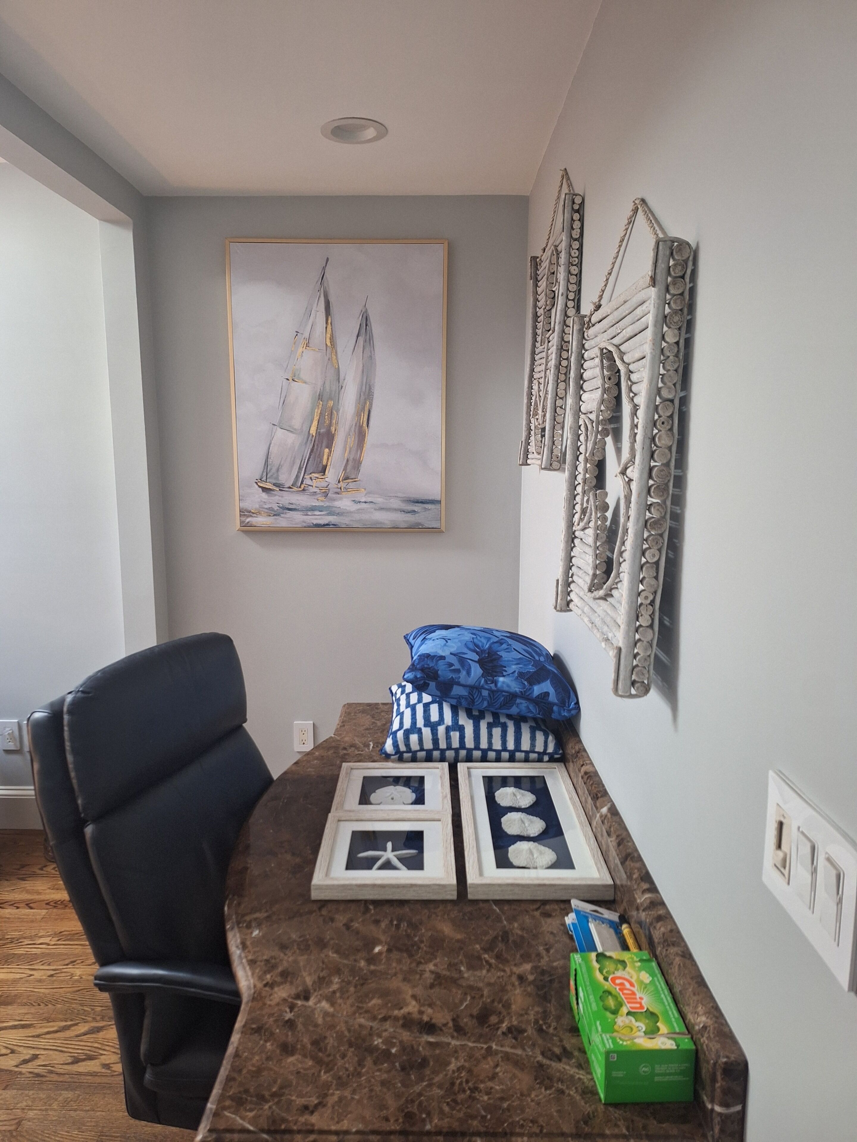 A room with a marble table, a framed sailboat painting, a black office chair, and a green box on the table.