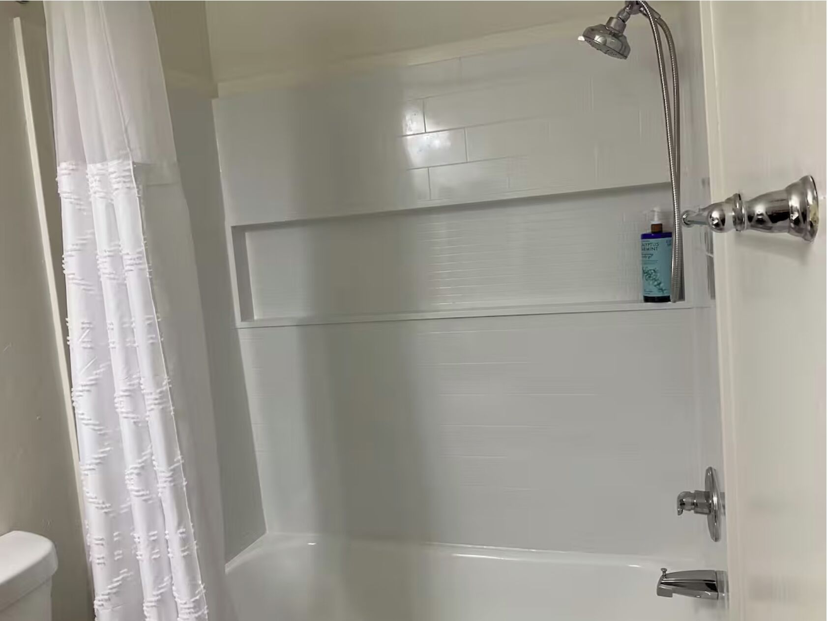 Un baño con una bañera blanca, un cabezal de ducha y un estante con artículos de aseo.