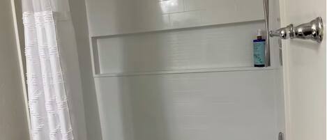 Un baño con una bañera blanca, un cabezal de ducha y un estante con artículos de aseo.
