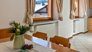A dining area with a table set for two, a vase with flowers, and a window with curtains.