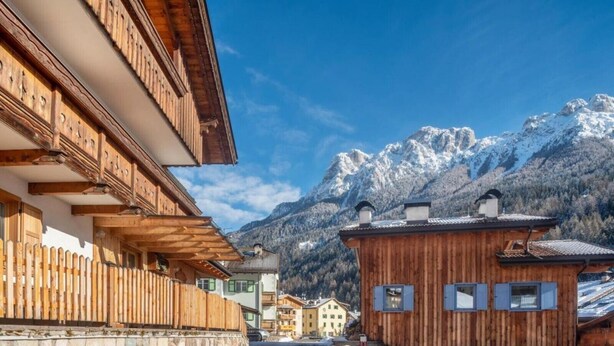 A wooden building with a stone wall and a wooden fence, set against a mountainous backdrop.