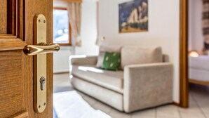 A wooden door with a brass handle, a beige sofa with a green pillow, and a painting on the wall.