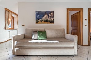 Une pièce avec un canapé beige, un tableau représentant un paysage de montagne, une porte en bois et un radiateur.