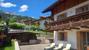 A traditional chalet with wooden balconies, a patio area with lounge chairs, and a view of a mountain.