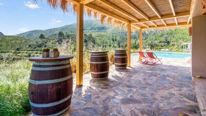 A covered outdoor area with stone flooring, wooden barrels, and red lounge chairs by a pool.