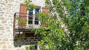 Ein Steinhaus mit Balkon, einem Fenster mit Rollläden und einem Baum im Vordergrund.