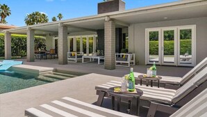 A poolside area with lounge chairs, a table, and a bottle of drink.