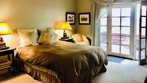 A bedroom with a large bed, two bedside tables with lamps, a chair, and a door leading to a balcony.