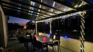 An outdoor patio area with a table and chairs, string lights, and a view of the sky. - Gîtes de France® - Chez Fanfan (Unknown)