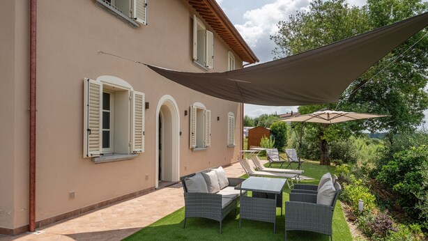 Una casa con patio, mobiliario exterior y una gran vela de sombra.