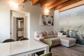 A modern living room with a sectional sofa, a dining table, and a mural on the wall.