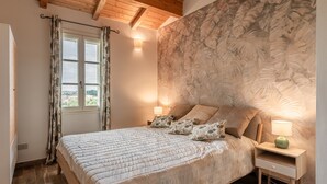 Un dormitorio con cama, mesitas de noche, una ventana con cortinas y una pared con un diseño de hojas.