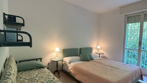 A hotel room with two beds, a small table, and a window with a view of greenery. - Splendido da aMare (Zoagli)