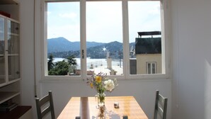 A dining area with a table and chairs, a vase with flowers, and a view of mountains and a body of water through large windows. - Splendido da aMare (Zoagli)