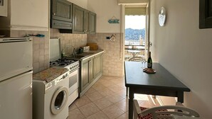 A compact kitchen with a washing machine, a stove, and cabinets. There's a dining table with chairs and a view of the outside. - Splendido da aMare (Zoagli)