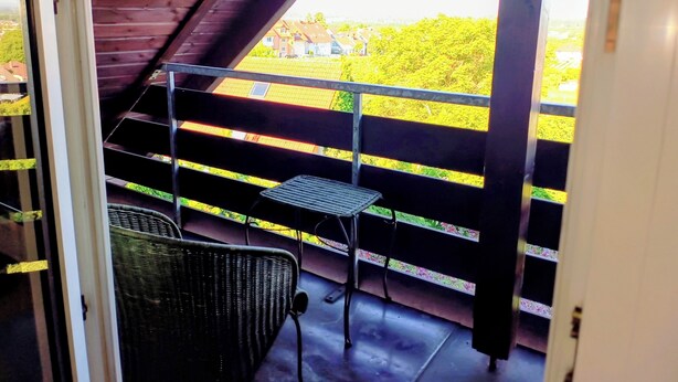 A balcony with a metal railing, a wicker chair, and a small table. - Wellness oasis in a wonderful panoramic location (Weinheim)