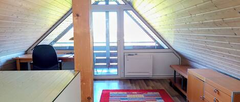 A room with a sloped ceiling, a desk, a chair, a radiator, and a colorful rug.