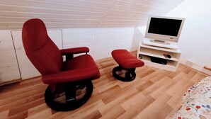 A room with a red chair, a television on a stand, and a bed with a floral bedspread. - Wellness oasis in a wonderful panoramic location (Weinheim)