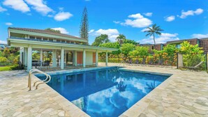 A swimming pool with a stone deck, a covered patio area, and a view of a residential building. - Charming 2-bedroom condo with AC, WiFi in delightful Princeville (Princeville)