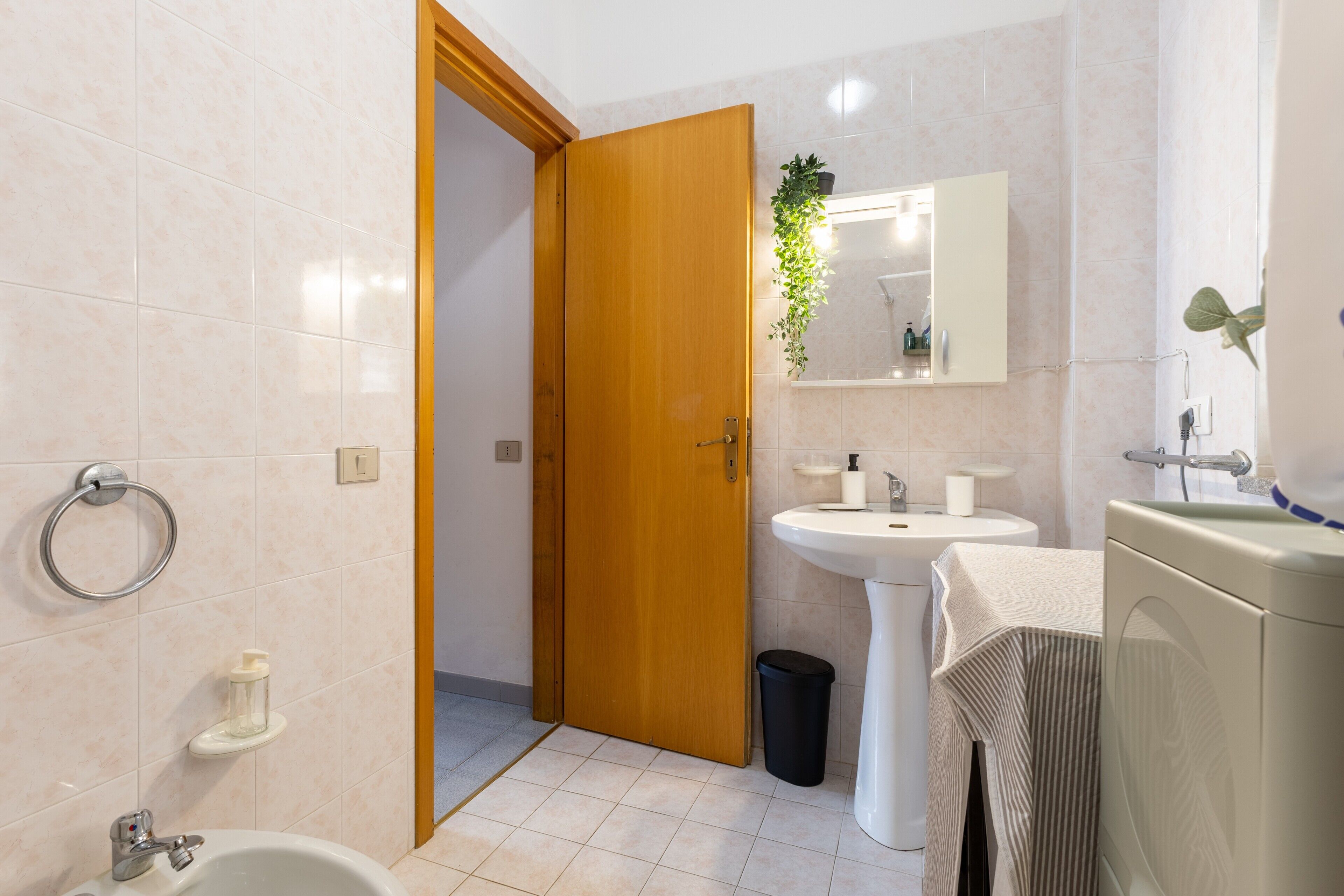 Une salle de bain comprenant des toilettes, un lavabo, un miroir et une porte donnant sur une autre pièce.