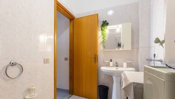 Une salle de bain comprenant des toilettes, un lavabo, un miroir et une porte donnant sur une autre pièce.