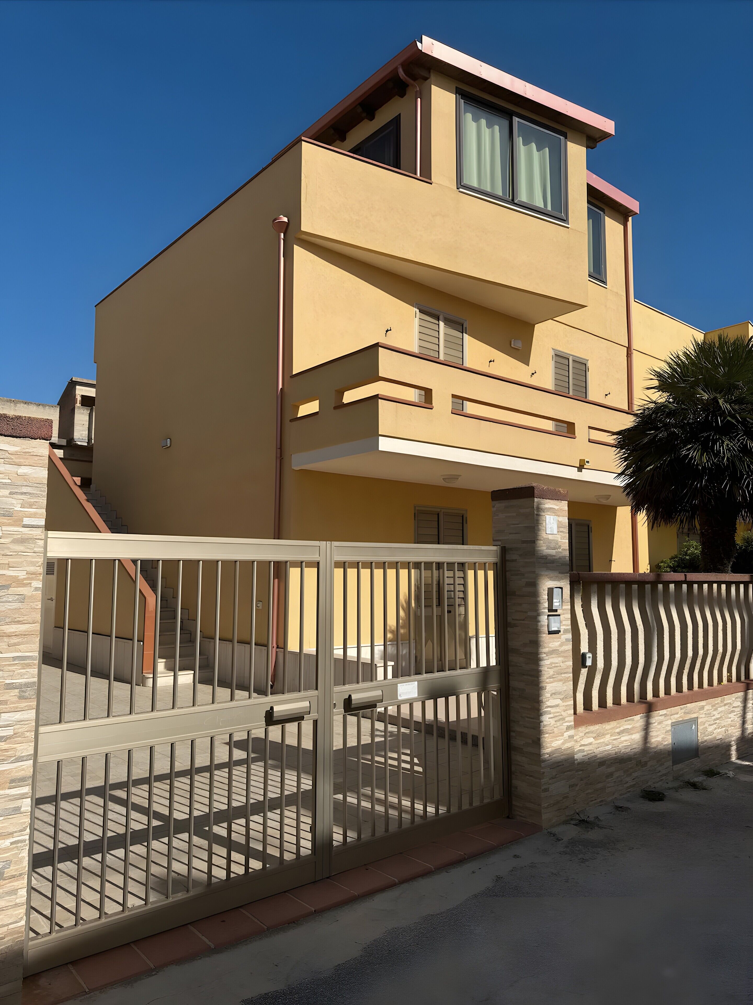 Un edificio moderno de dos pisos con entrada protegida por una reja, una escalera y un balcón.